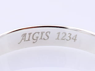 「AIGIS 1234」と刻印されたシルバーリングで、ブランド名やシリアルナンバーが彫られている可能性がある。