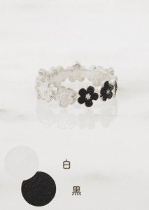 Clear floral bracelet with alternating white and black flowers displayed on a reflective surface; labels show white (白) and black (黑).